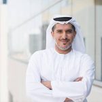 A photo of confident and smiling mid adult arab businessman. Emirati man is wearing tradition clothing. Portrait of middle eastern professional standing arms with crossed outside office building. Dubai, United Arab Emirates, Middle East